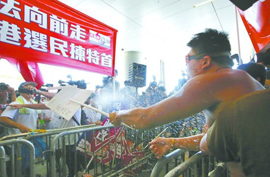 17日，在香港立法會外，一名反對政改的男子向支持派人群投擲標牌。
