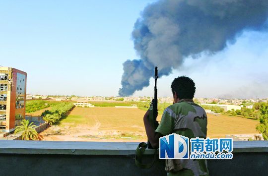 2日，利比亞首都的黎波里，一民兵武裝成員眺望被火箭彈擊中的儲油罐冒出濃煙。
