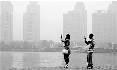 29日中午，鄭東新區(qū)如意湖畔，兩個年輕人拍攝霧霾中的景色。 鄭州晚報記者 馬健 圖