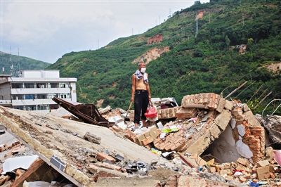 8月9日,龍頭山鎮,一位老者在自家房屋廢墟上尋找家當。